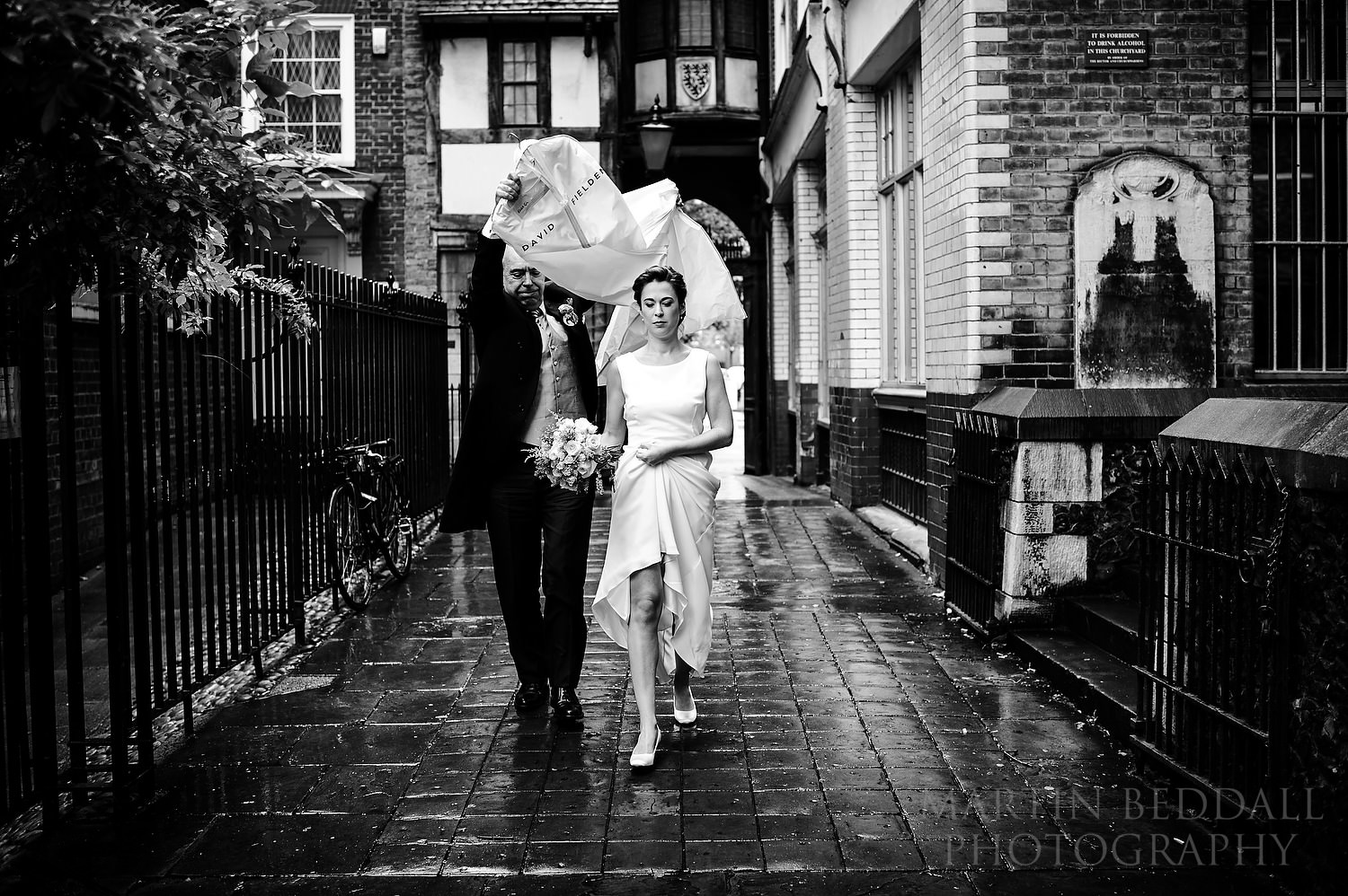 Bride's father tries to keep the rain off with a bag