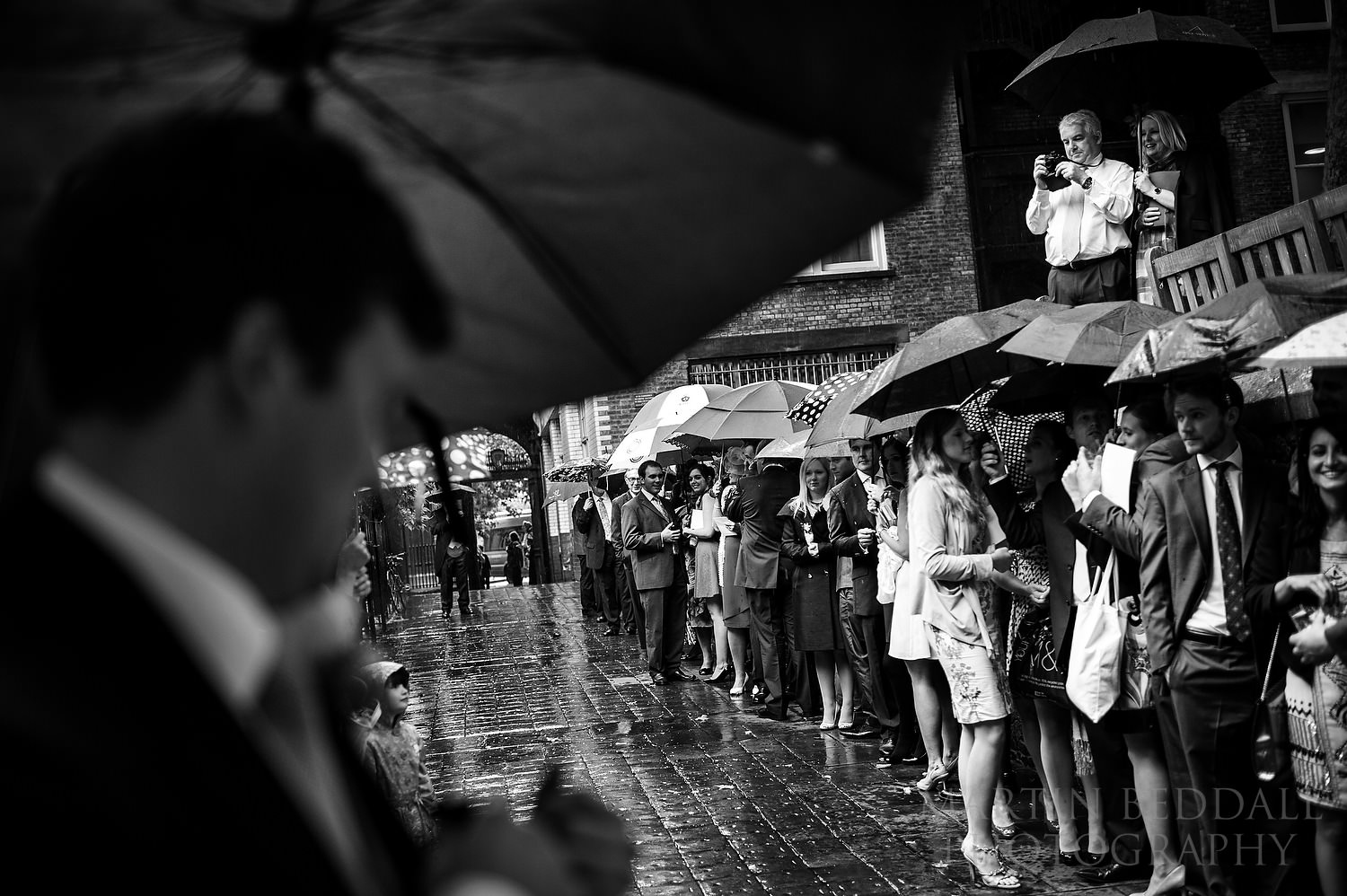Wedding guests line up in the rain for confetti at St Bartholomew the Great Church