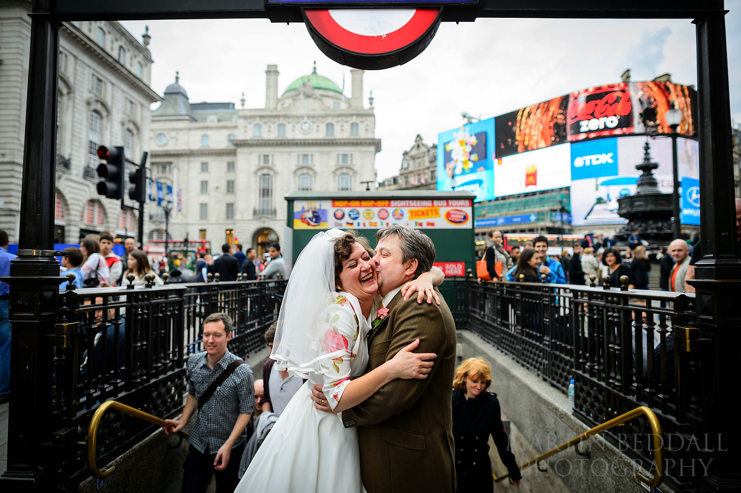 Bride and groom embrace outside Tube exit