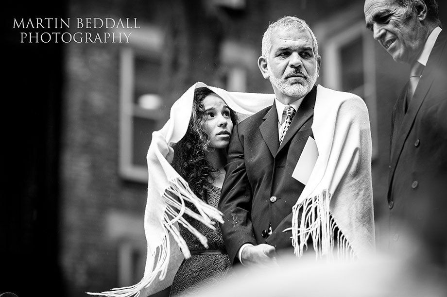 Wedding guests shelter fron the rain as they wait for the couple