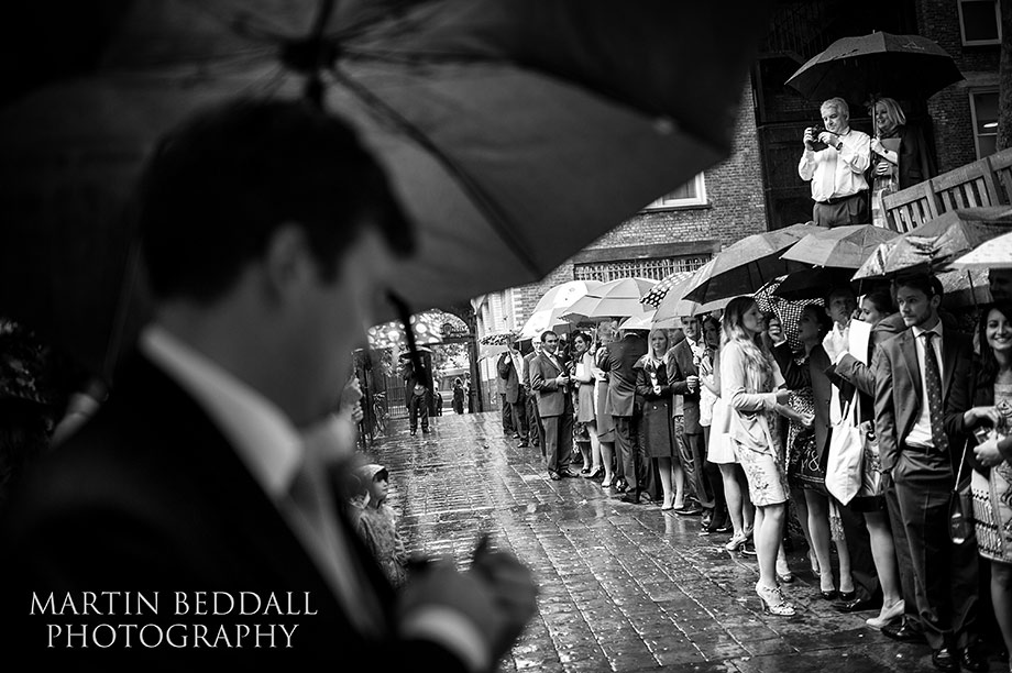 Wedding guests shelter fron the rain as they wait for the couple to exit the church