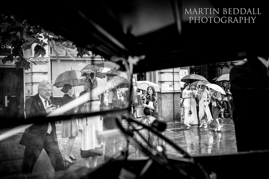 Wedding guests and umbrellas viewed through the wedding car