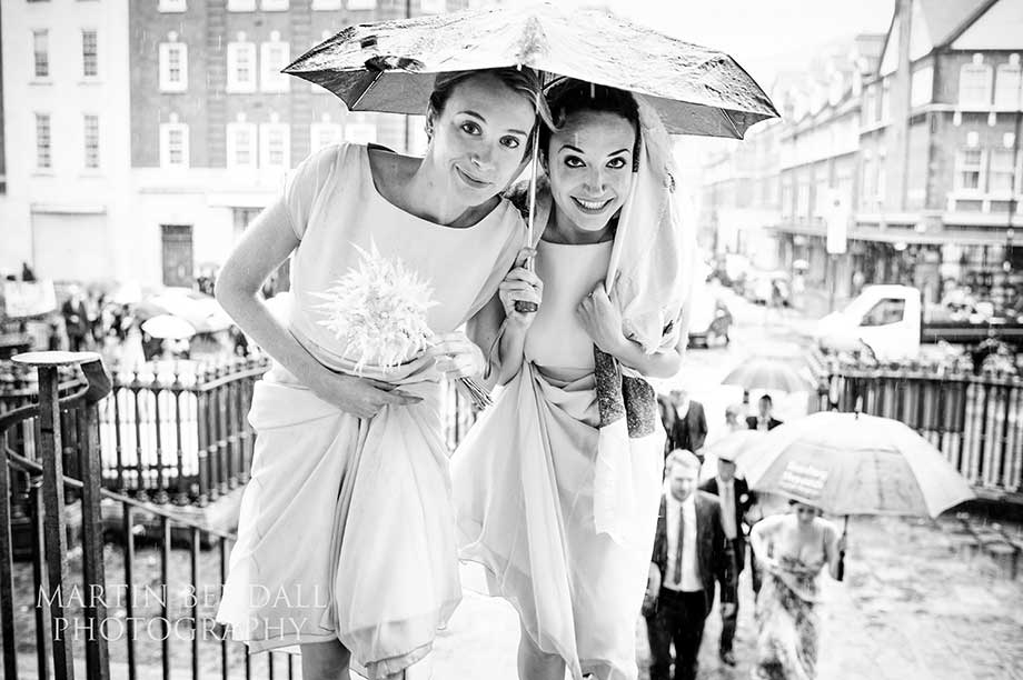 Two bridesmaids under an umbrella as they rain pours down