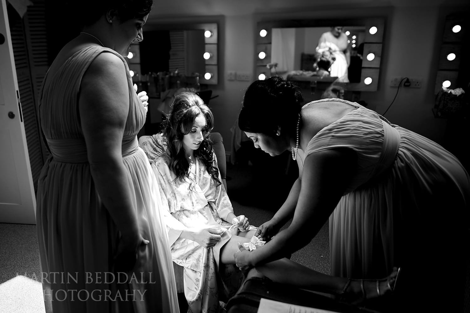 Bridesmaids help the bride with her garter at Millbridge Court