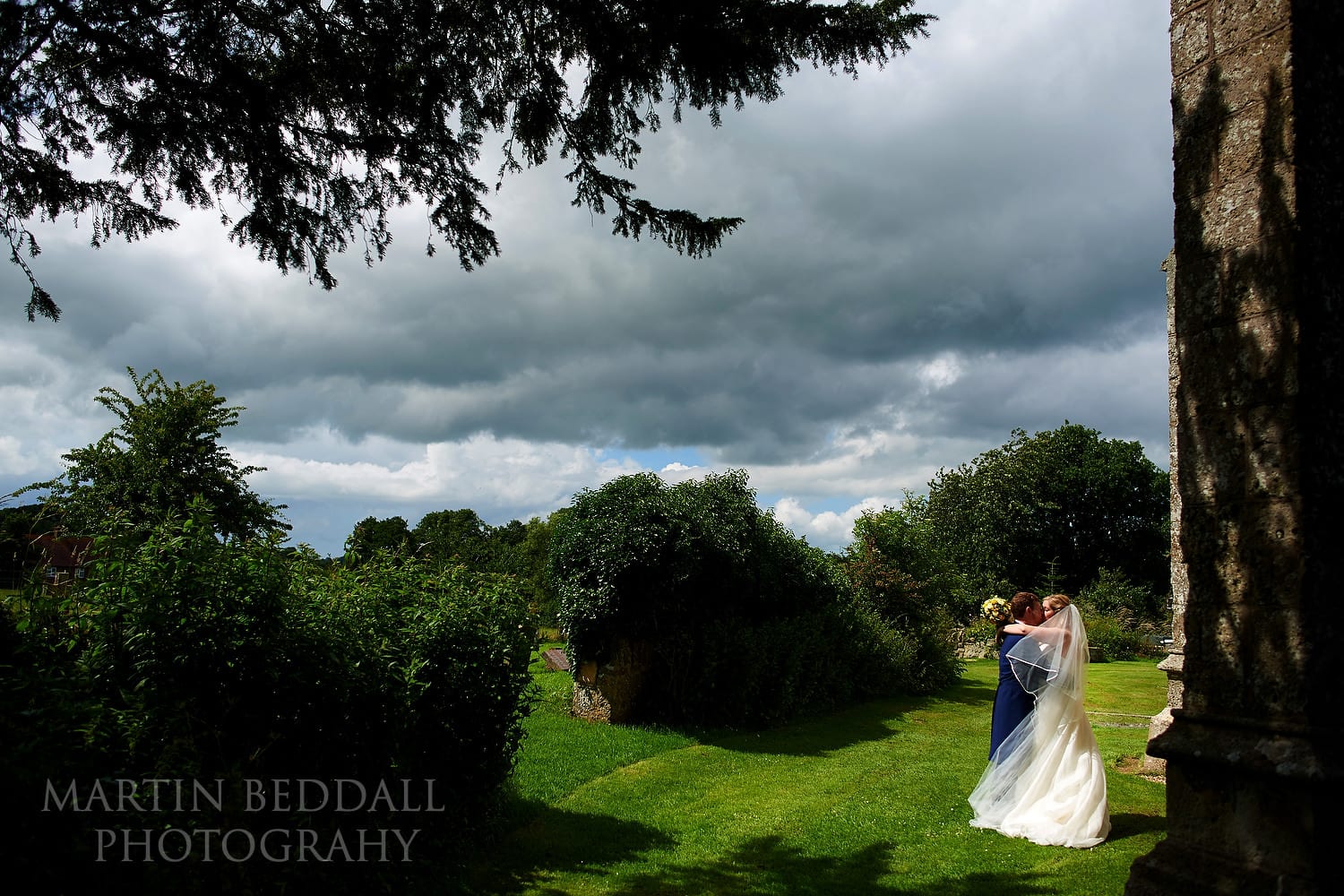 Bride and groom kiss around the side of the church